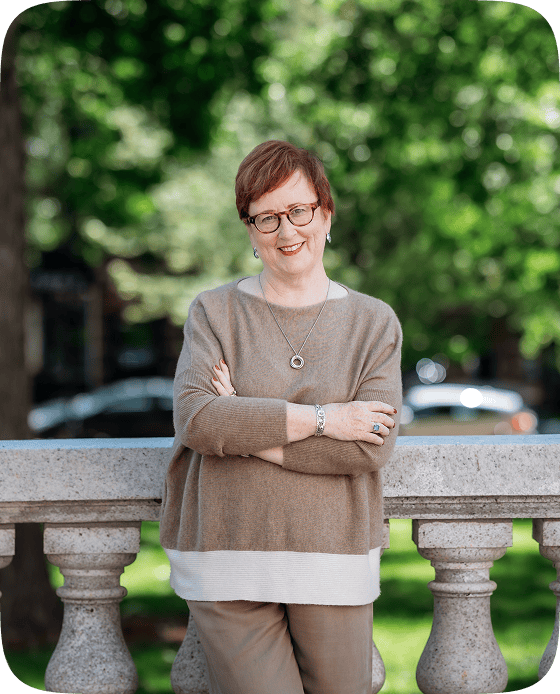 Kathleen Quinn standing outdoors with arms crossed, smiling confidently in a neutral-toned outfit, representing warmth, professionalism, and authenticity.