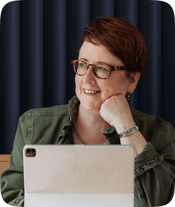 Kathleen Quinn smiling while seated at her desk with a laptop, conveying approachability, confidence, and leadership.